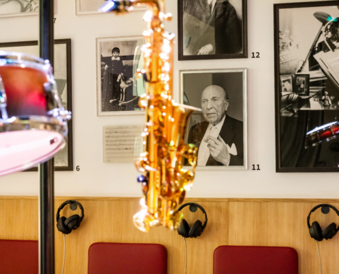 Nahaufnahme aus der Lebensbühne. Im Vordergrund hängt ein Saxophon, im Hintergrund hängen Fotografien von Robert Stolz an der Wand.